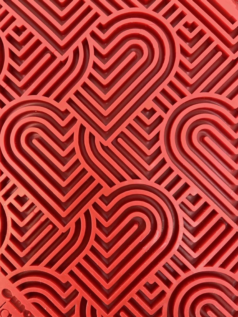 Red heart-patterned silicone mat with geometric design for slow feeding and mental stimulation.